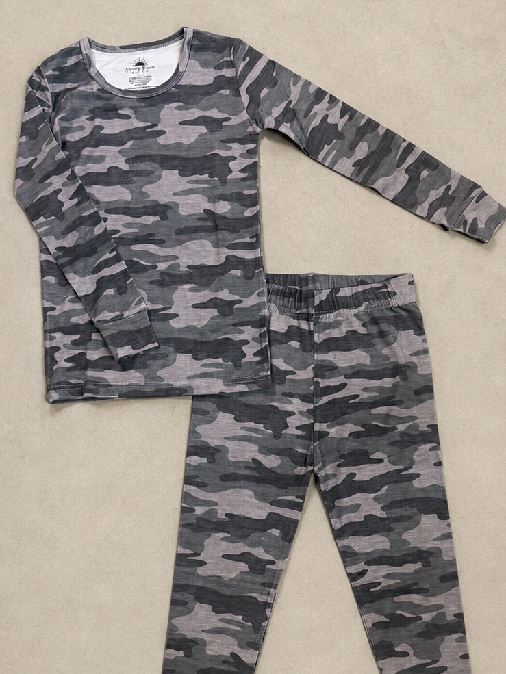 A two-piece children's pajama set featuring a long-sleeve top and matching pants in a gray and black camouflage pattern, laid flat on a beige textured background.