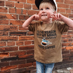 Child wearing a brown coffee t-shirt standing against a brick wall