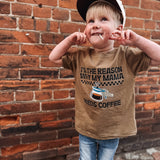 Child wearing a brown coffee t-shirt standing against a brick wall