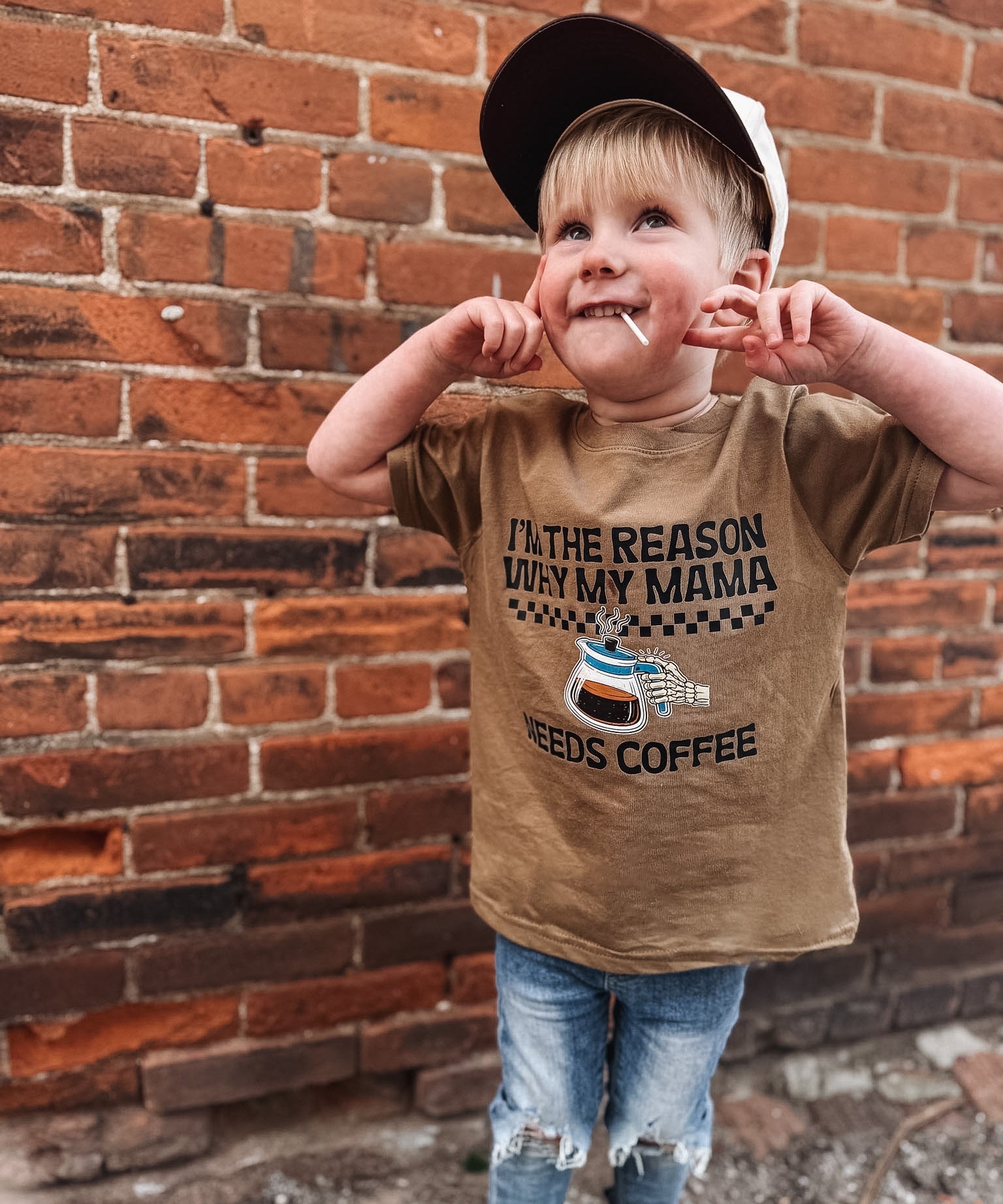 Child wearing a brown coffee t-shirt standing against a brick wall