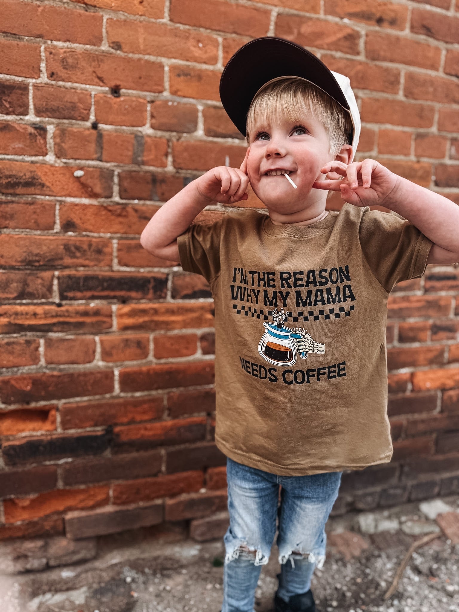 Child wearing a brown coffee t-shirt standing against a brick wall