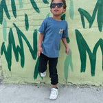 Child wearing sunglasses and a blue shirt standing in front of a green mural.
