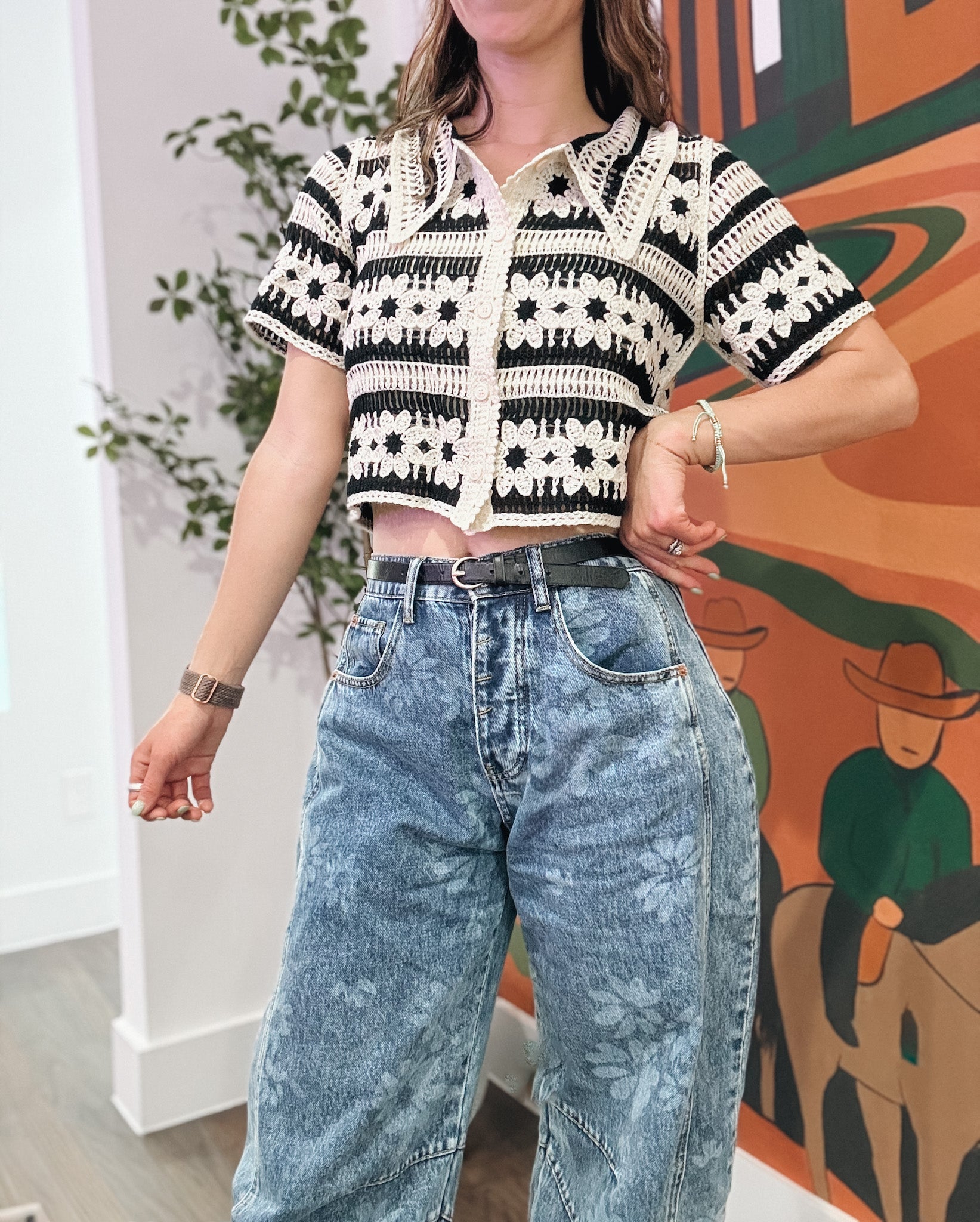 Person wearing a black and white patterned top with acid-wash jeans in front of a colorful mural.