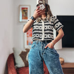 Person wearing a black and white patterned shirt and blue jeans taking a mirror selfie.