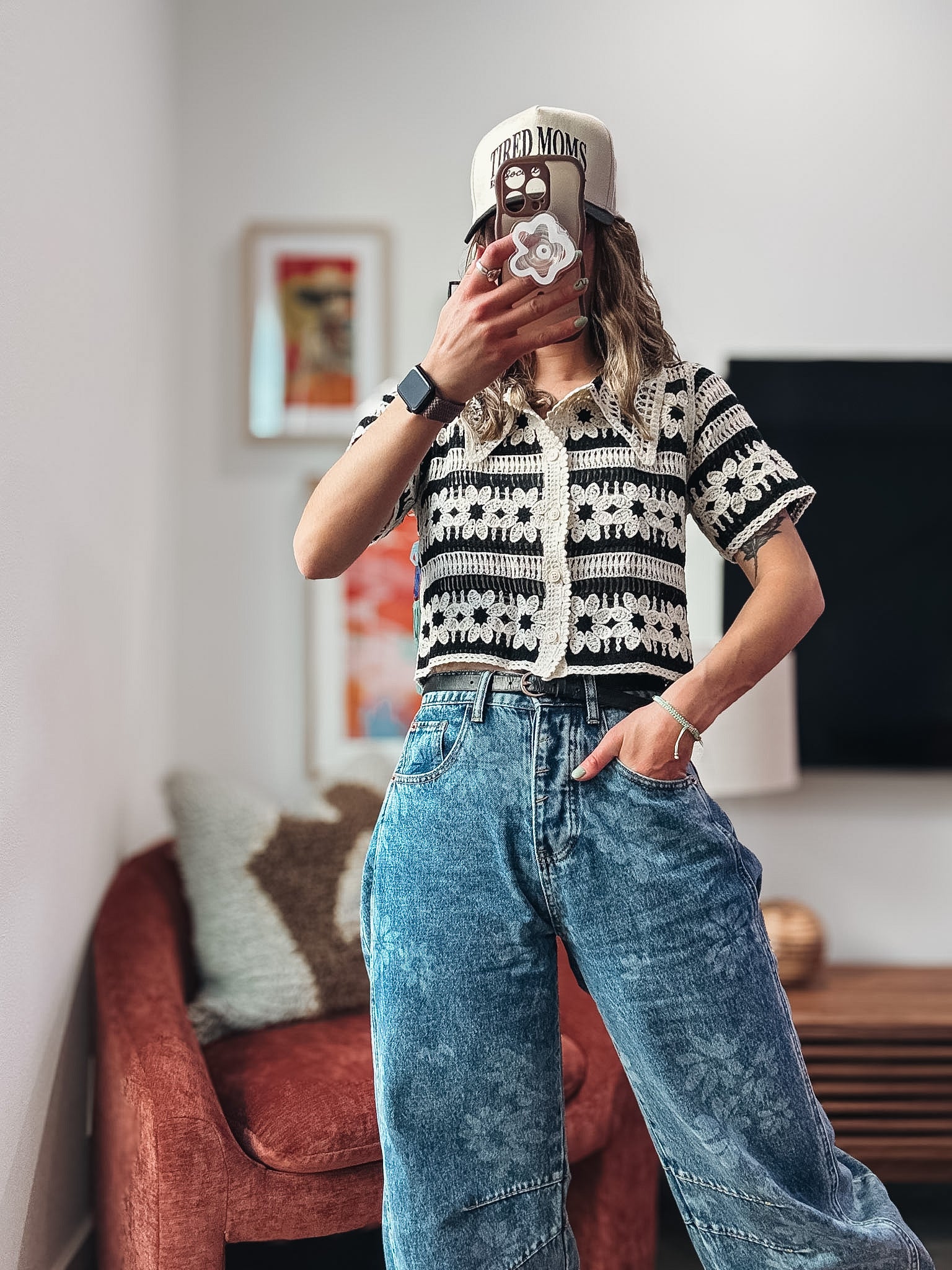 Person wearing a black and white patterned shirt and blue jeans taking a mirror selfie.