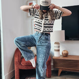 Person wearing a patterned shirt and jeans in a living room setting