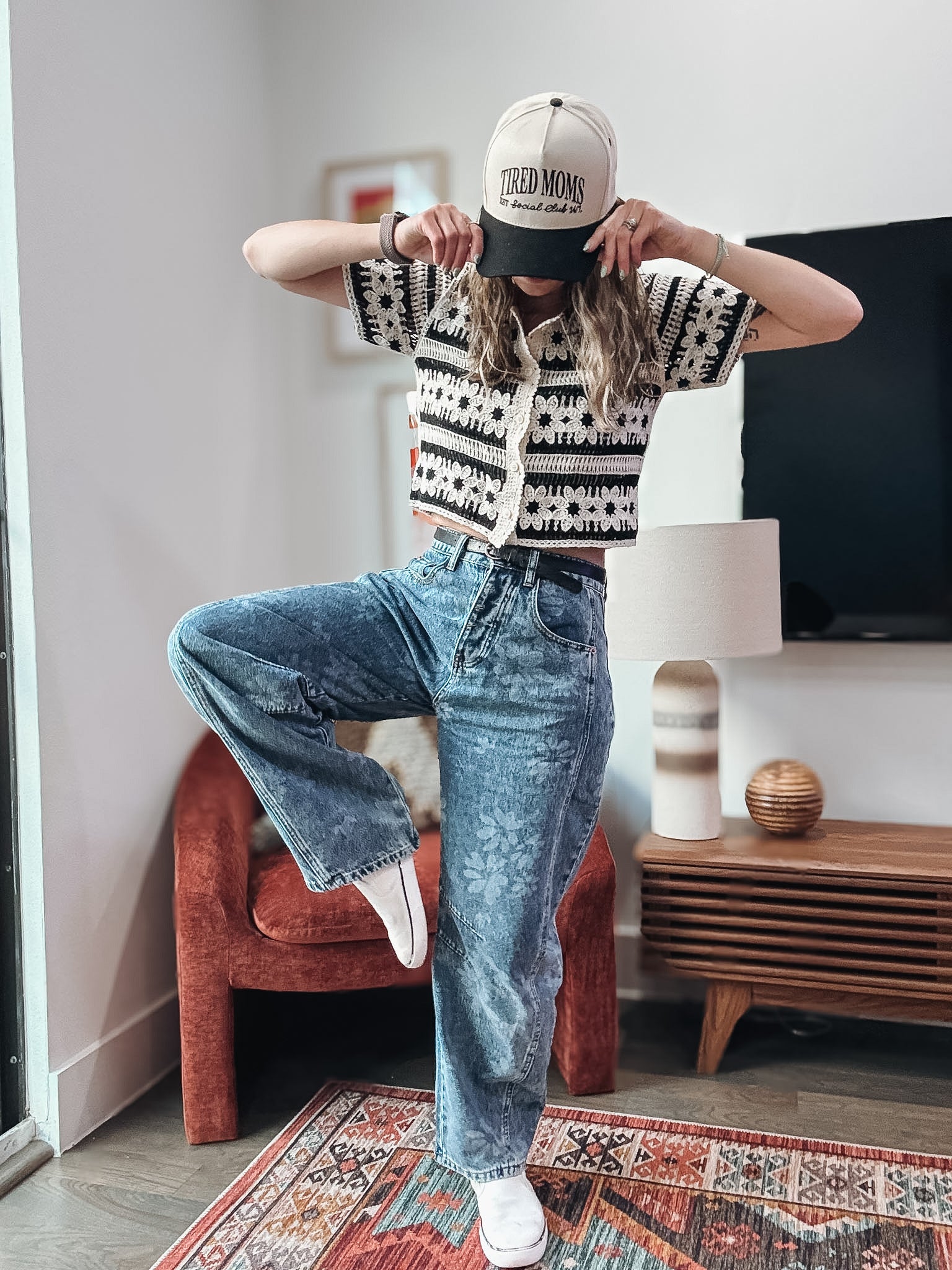 Person wearing a patterned shirt and jeans in a living room setting