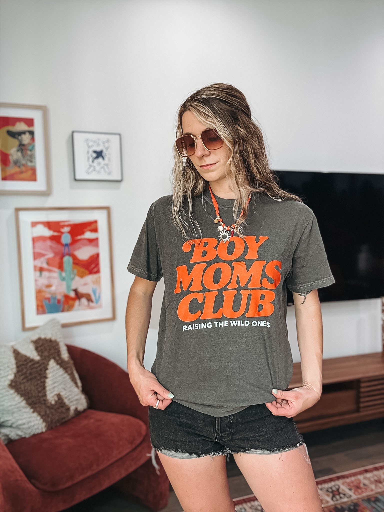 Woman wearing a 'Boy Moms Club' t-shirt in a living room setting