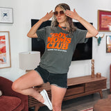 Woman wearing a 'Boy Moms Club' t-shirt in a living room.