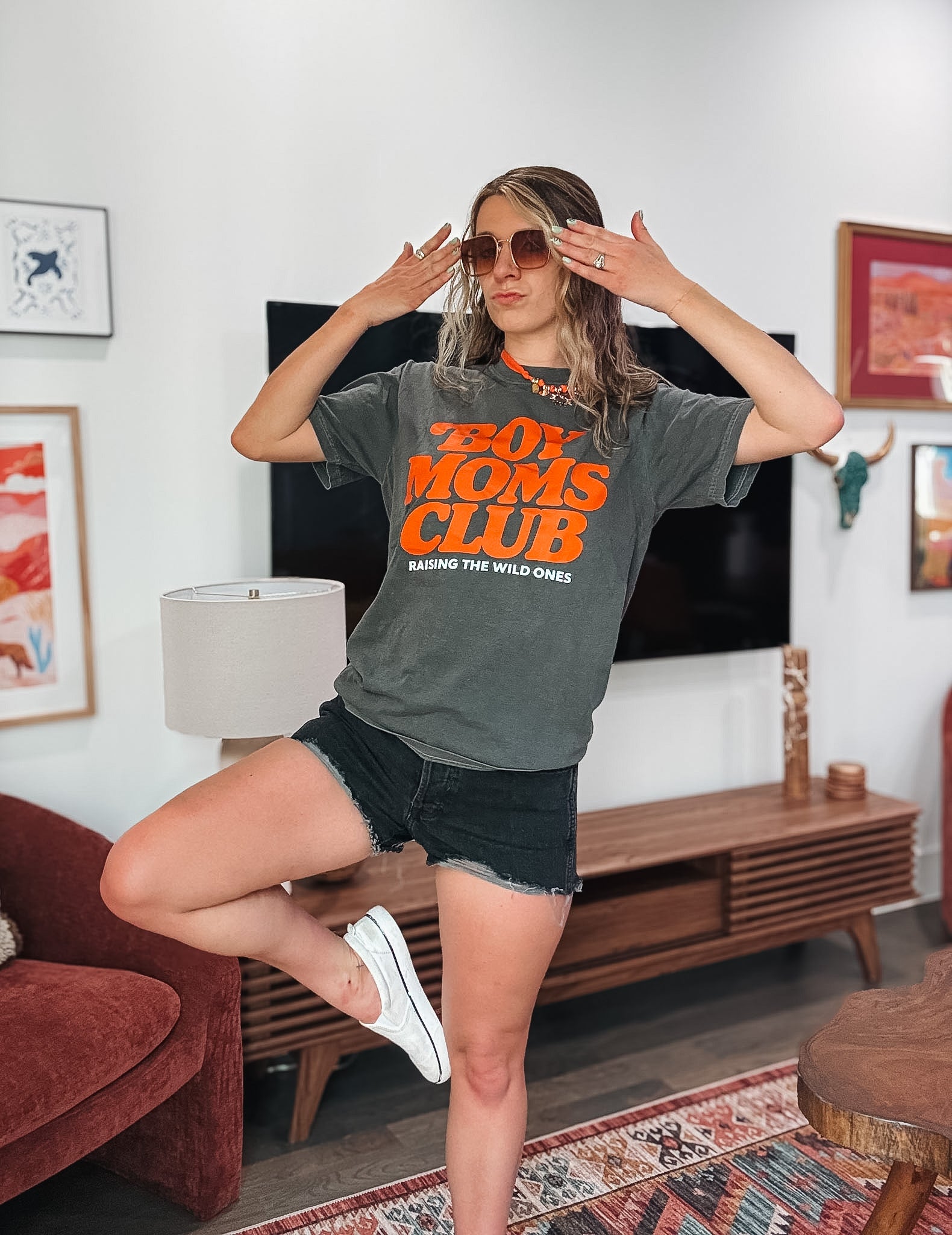 Woman wearing a 'Boy Moms Club' t-shirt in a living room.