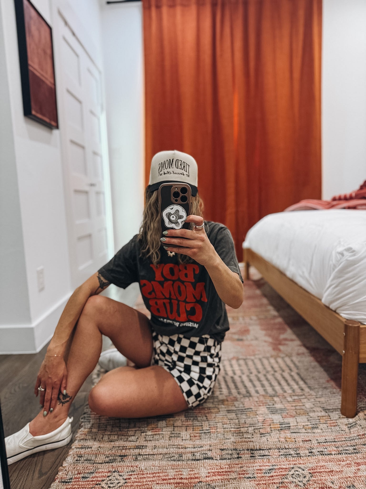 Person taking a mirror selfie in a room with a bed and wooden floor.