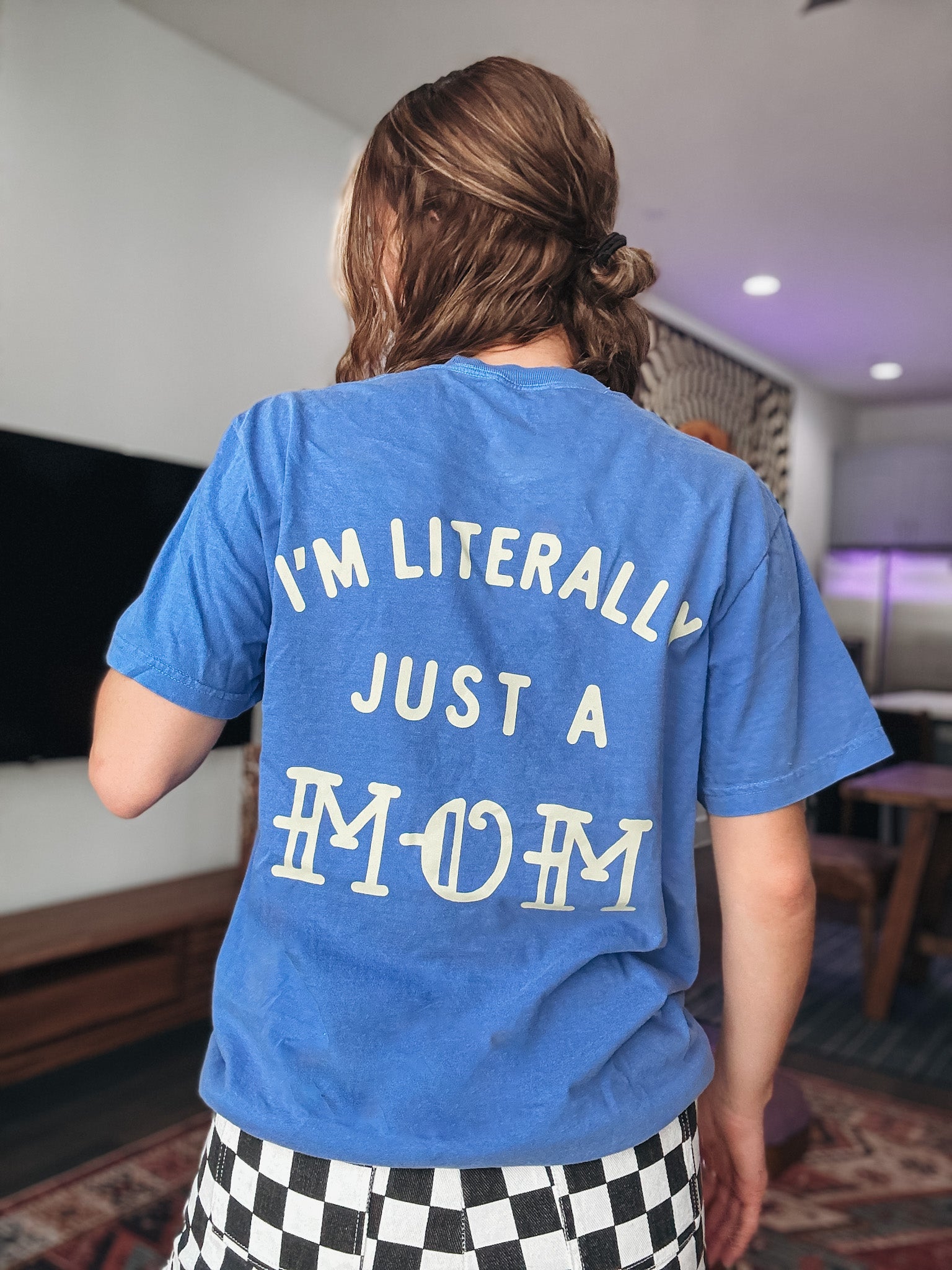 Person wearing a blue t-shirt with text on the back in a room.