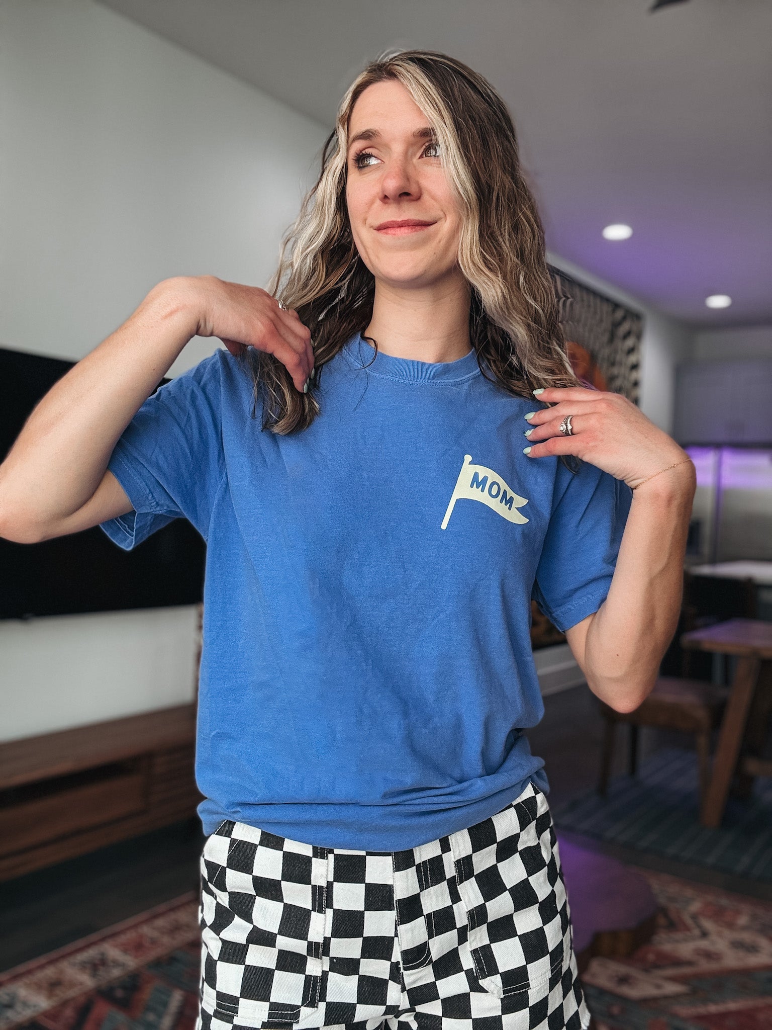Person wearing a blue t-shirt with a 'mom' flag design in a room.