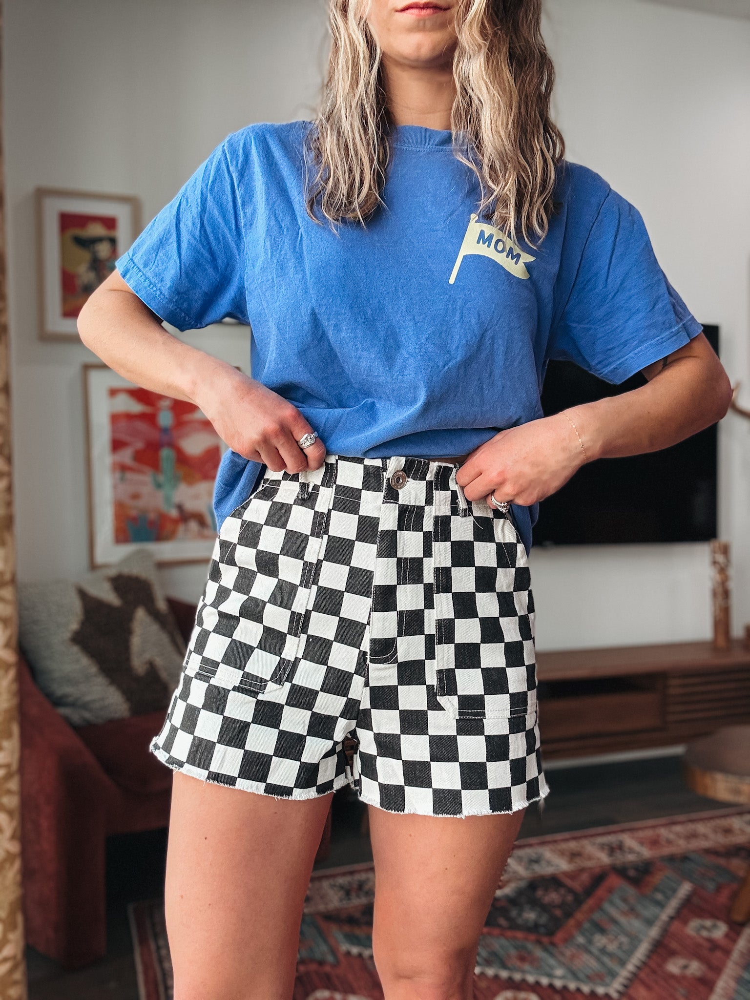Person wearing a blue t-shirt with text and checkered shorts in an indoor setting