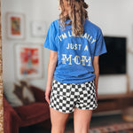 Person wearing a blue t-shirt with text and checkered shorts in a room.