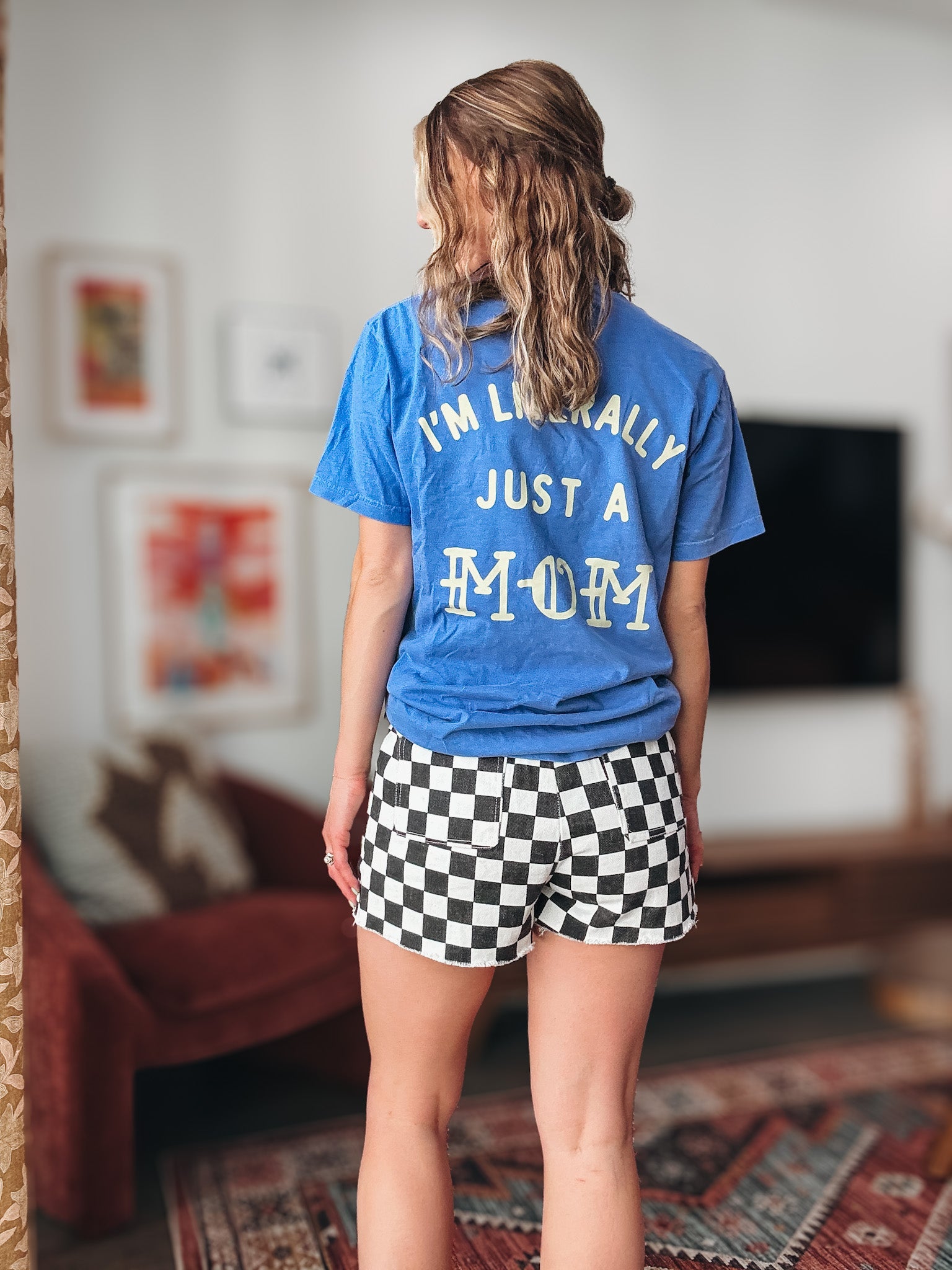 Person wearing a blue t-shirt with text and checkered shorts in a room.