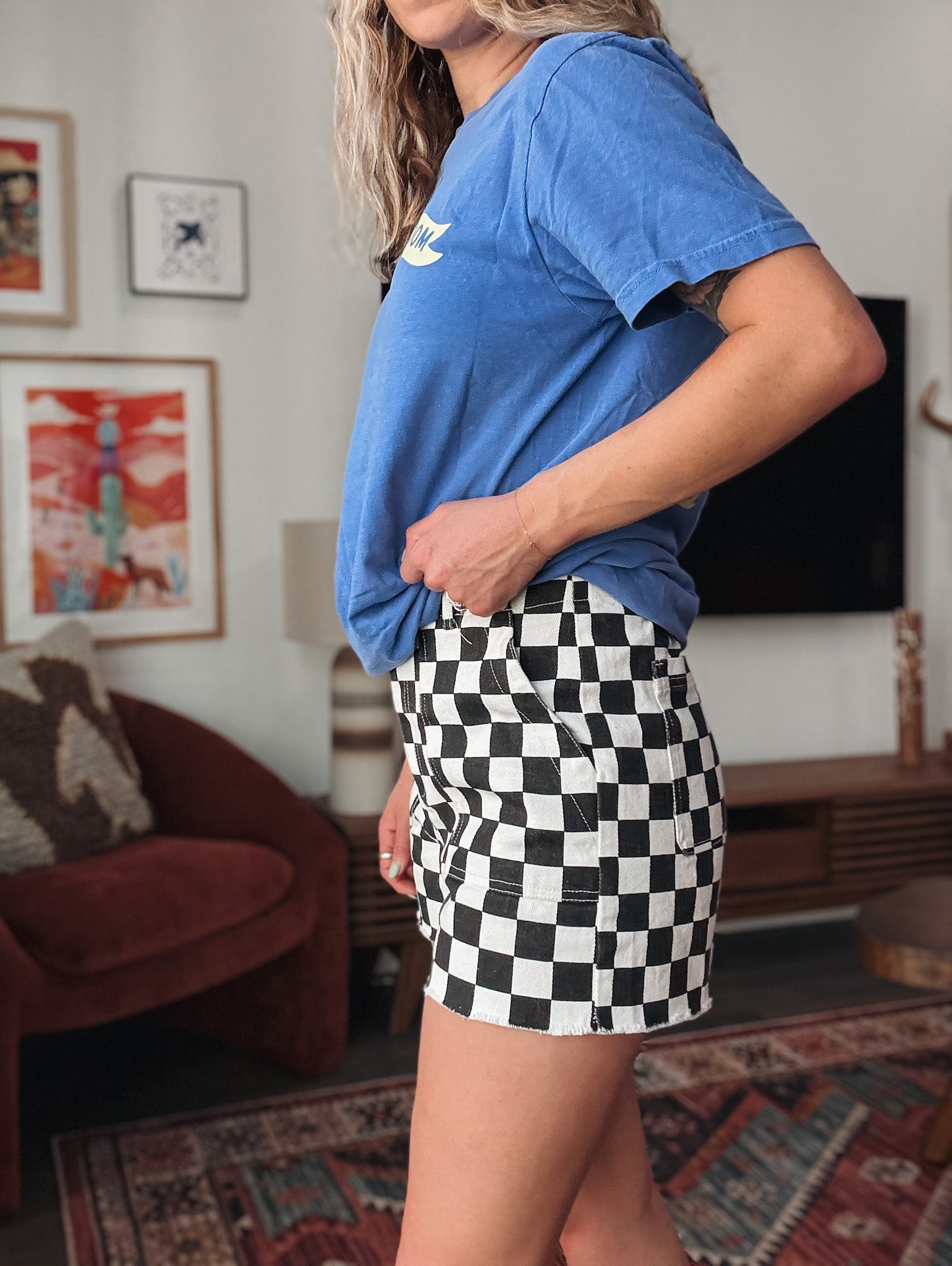 Person wearing a blue t-shirt and black and white checkered shorts in a living room.