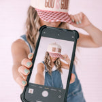 Person wearing a 'GOD IS GOOD' cap, holding a phone with a similar cap displayed on the screen.