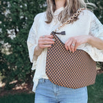 Woman outdoors holding a brown and black checkered slouchy shoulder purse. 
