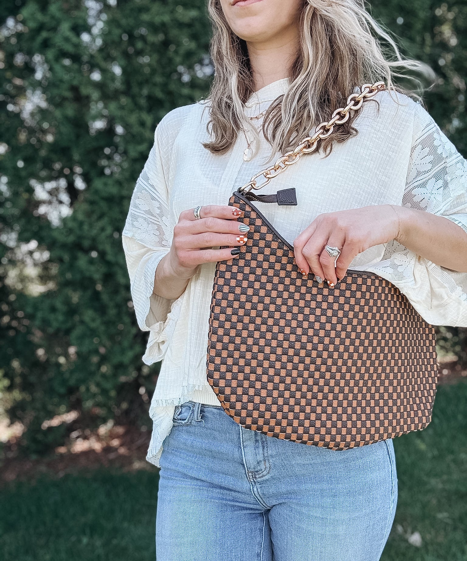 Woman outdoors holding a brown and black checkered slouchy shoulder purse. 