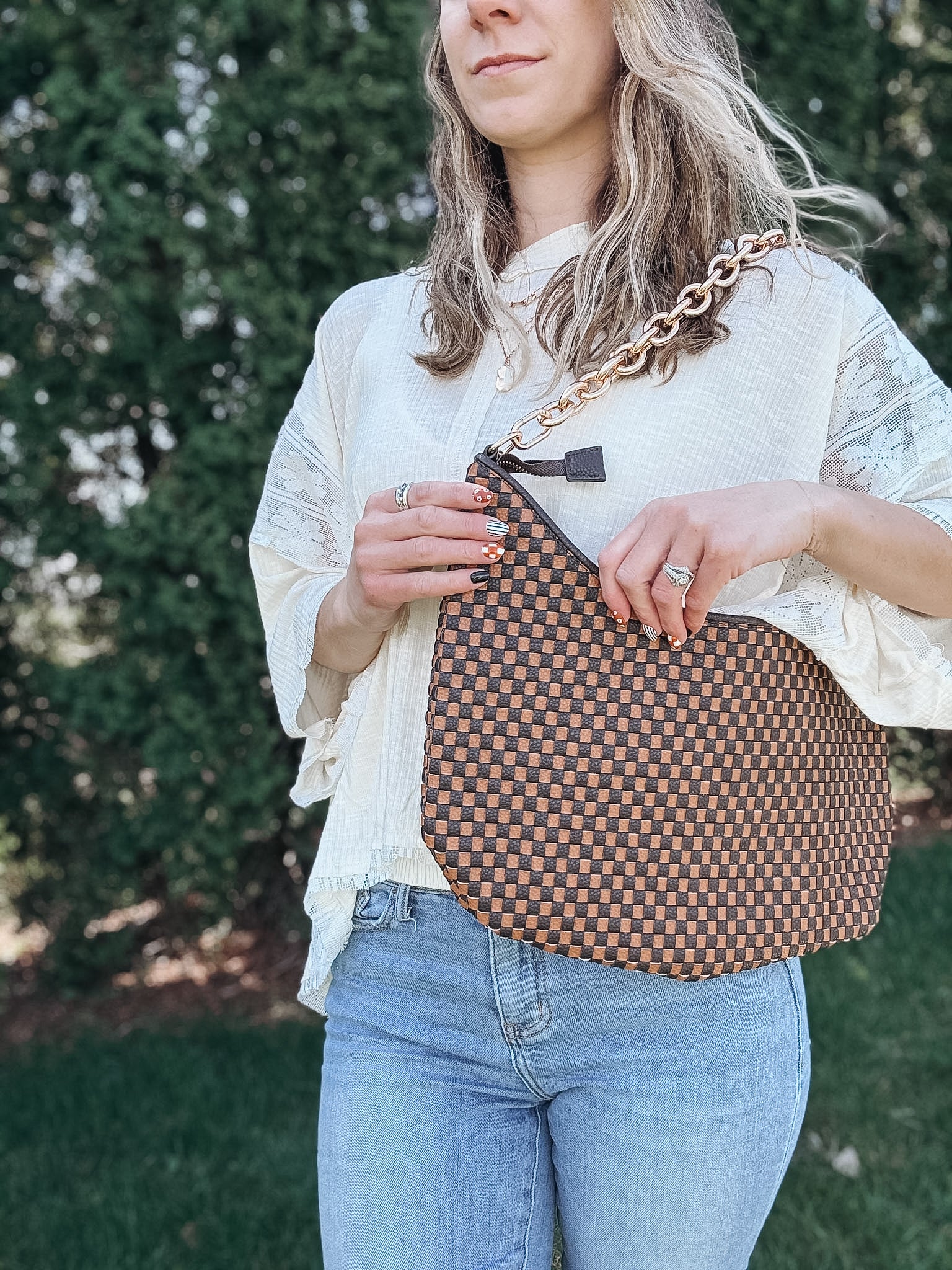 Woman outdoors holding a brown and black checkered slouchy shoulder purse. 