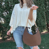 Woman outdoors holding a brown and black checkered slouchy shoulder purse. 