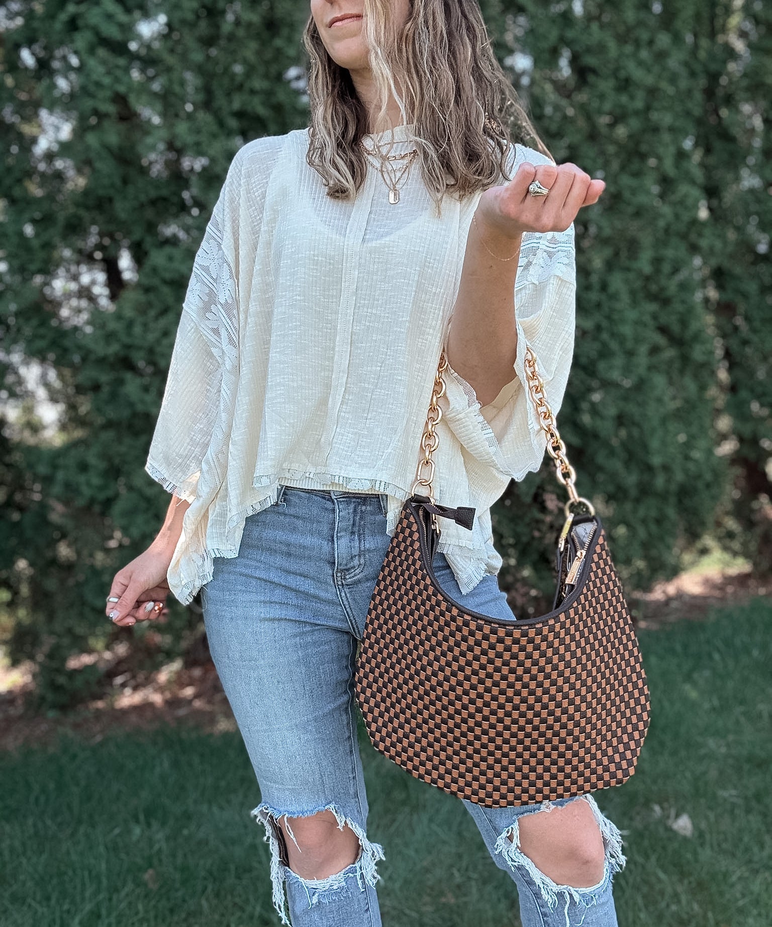 Woman outdoors holding a brown and black checkered slouchy shoulder purse. 