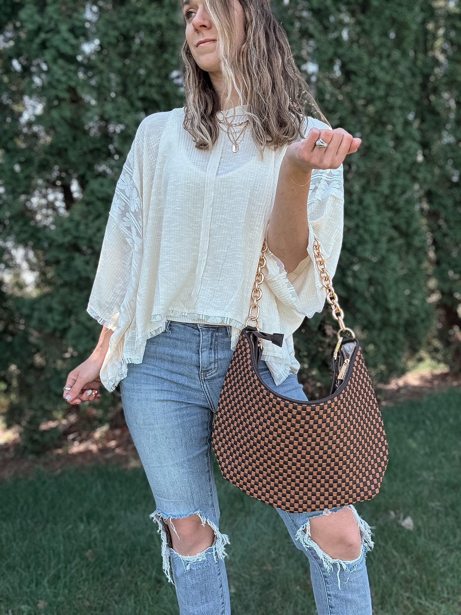 Woman outdoors holding a brown and black checkered slouchy shoulder purse. 