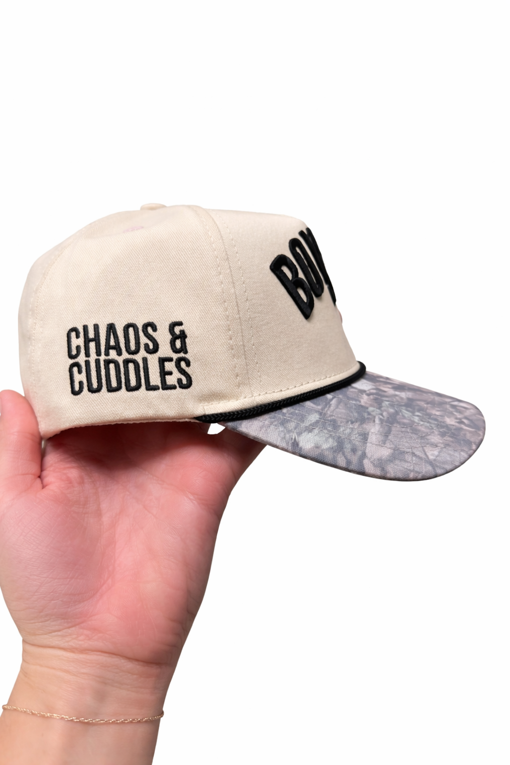 Beige cap with text 'Chaos & Cuddles' on the side held by a hand on a white background
