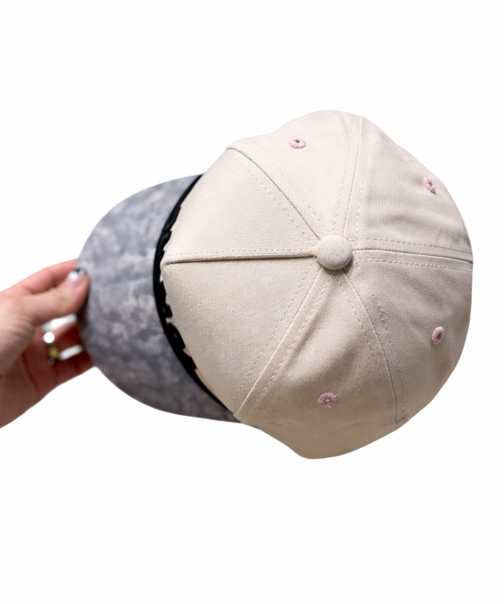 Beige cap with pink buttons held by a hand on a white background