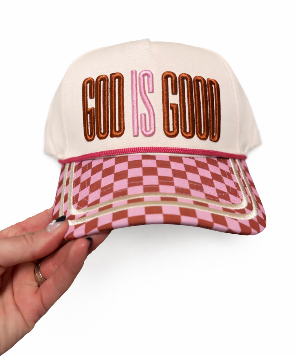 Cap with 'God is Good' text and checkered pattern held by a hand on a white background