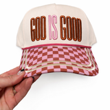 Cap with 'God is Good' text and checkered pattern held by a hand on a white background