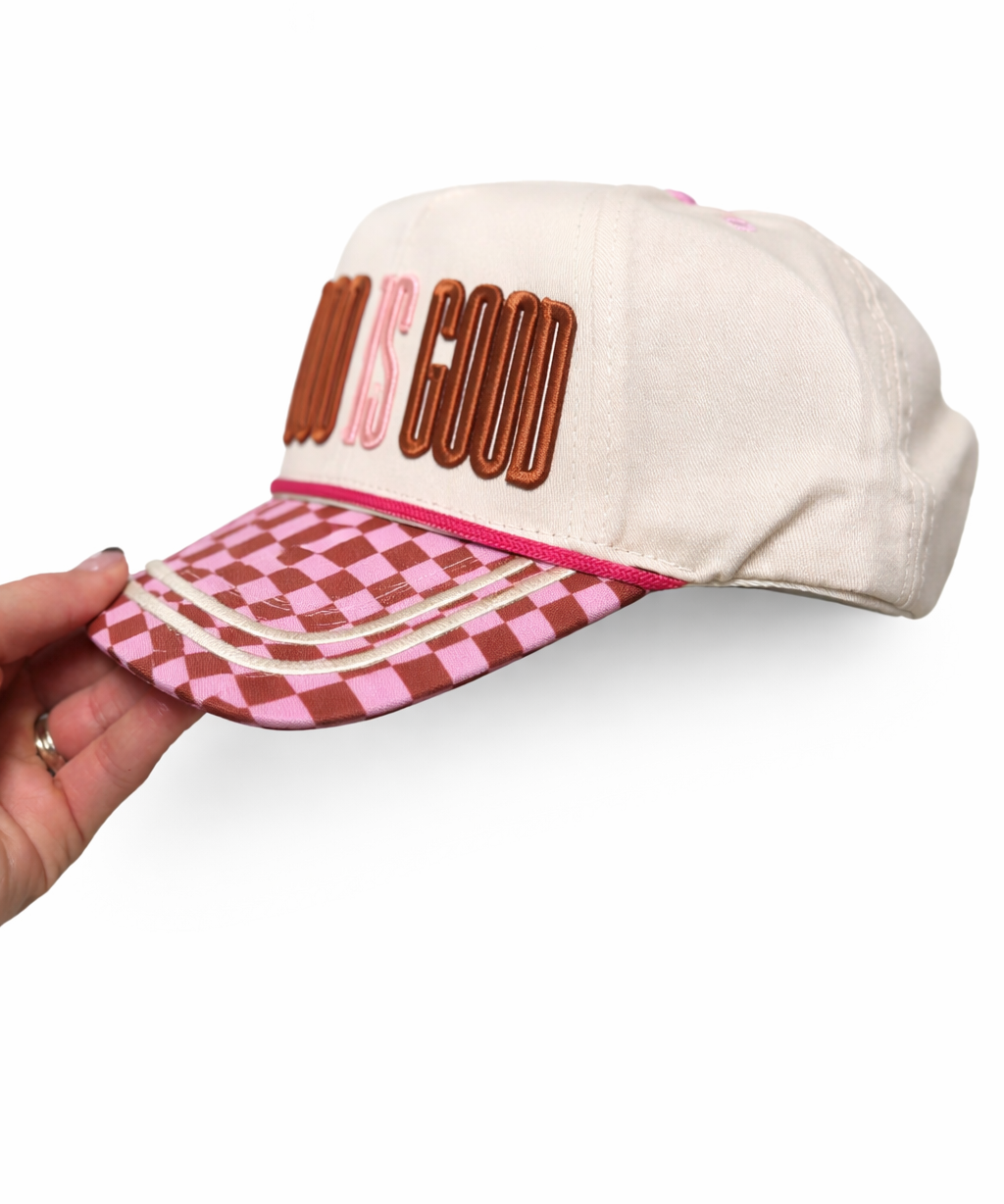 Cap with 'God is Good' text and checkered brim held by a hand on a white background