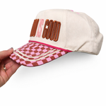 Cap with 'God is Good' text and checkered brim held by a hand on a white background