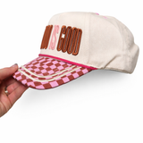 Cap with 'God is Good' text and checkered brim held by a hand on a white background