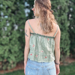 Woman wearing a green floral top and blue jeans standing in front of greenery