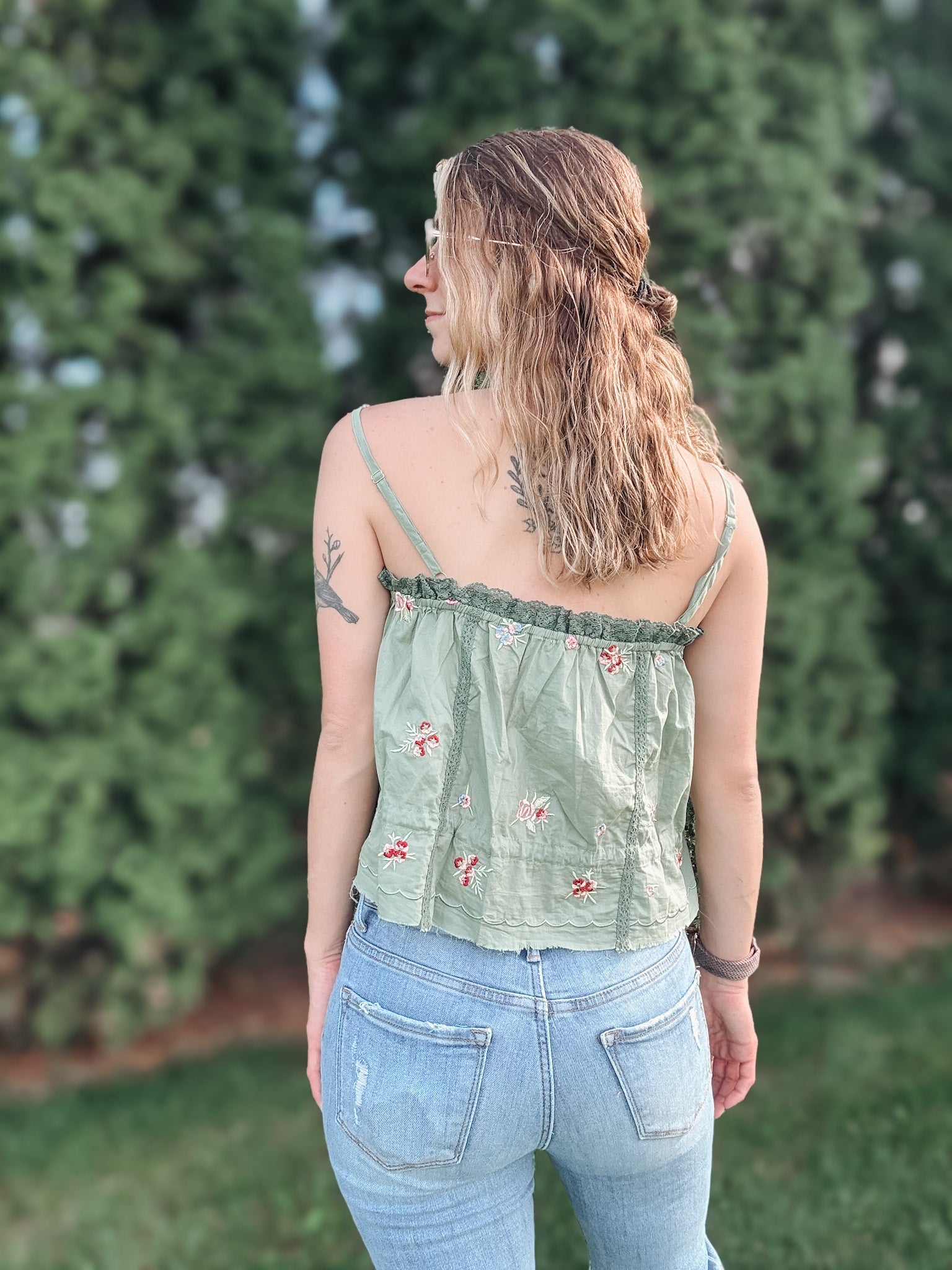 Woman wearing a green floral top and blue jeans standing in front of greenery