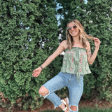 Woman in a green top and blue jeans posing outdoors with greenery in the background