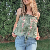 Woman wearing a green embroidered top and blue jeans outdoors.
