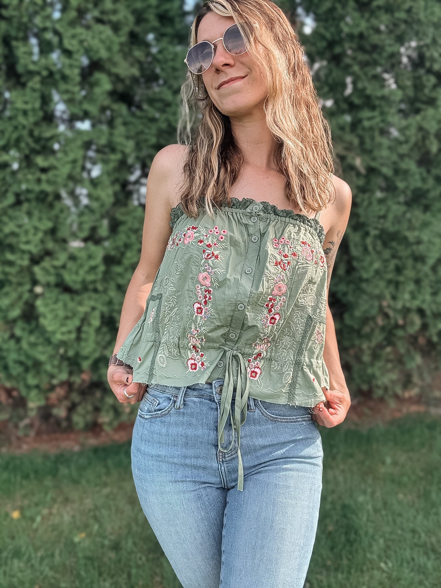 Woman wearing a green embroidered top and blue jeans outdoors.
