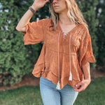 Woman wearing a rust-colored top with tassels and light blue jeans outdoors.