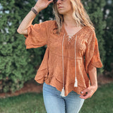 Woman wearing a rust-colored top with tassels and light blue jeans outdoors.