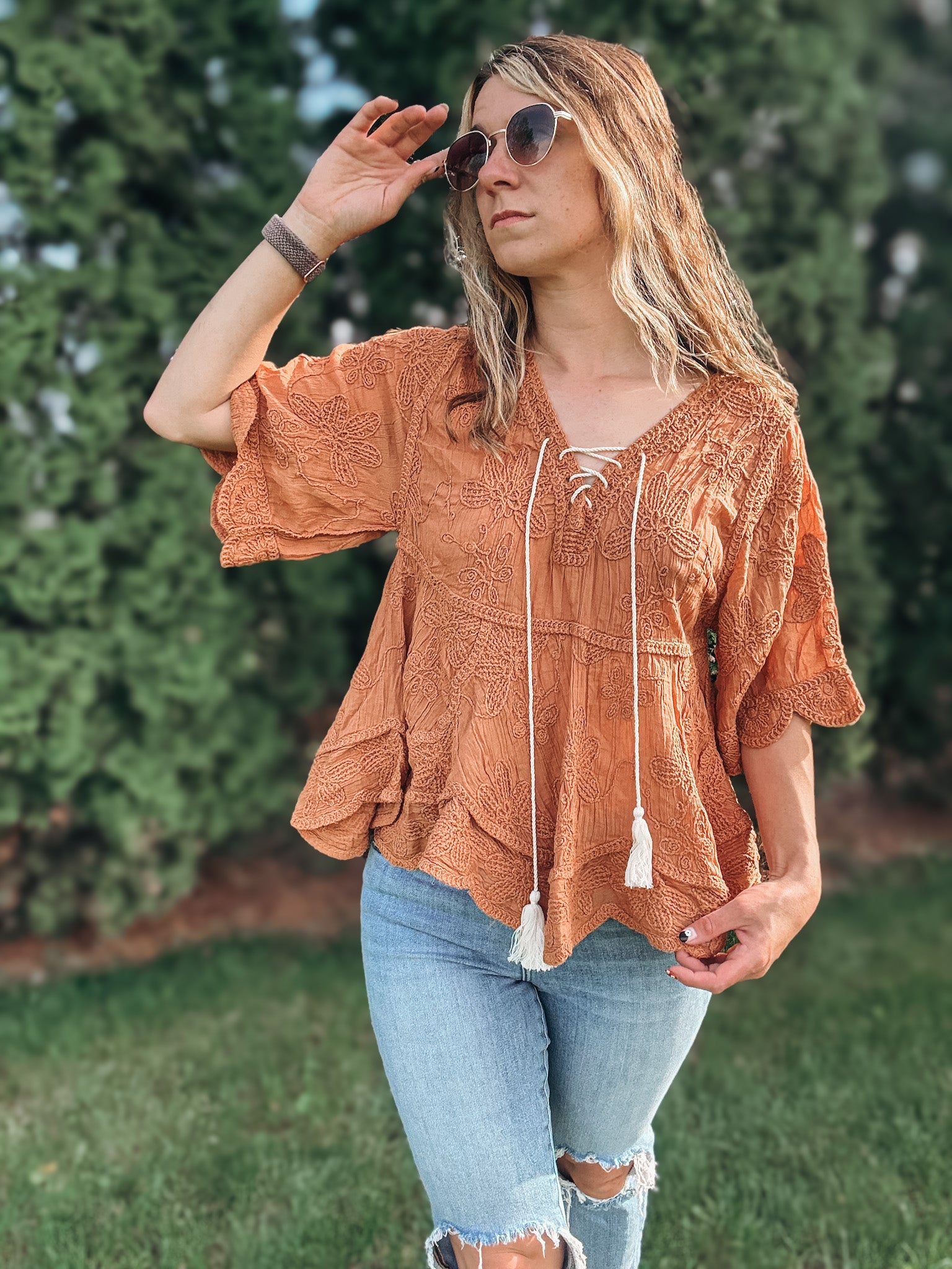 Woman wearing a rust-colored top with tassels and light blue jeans outdoors.