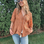 Woman wearing a brown lace top and ripped jeans standing outdoors with greenery in the background
