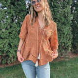 Woman wearing a brown lace top and ripped jeans standing outdoors with greenery in the background