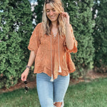 Woman wearing an orange lace top and ripped jeans standing outdoors with greenery in the background
