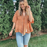 Woman wearing an orange lace top and ripped jeans standing outdoors with greenery in the background