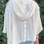 Person wearing a light-colored cardigan over a white shirt with a blurred green background