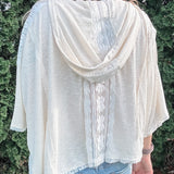 Person wearing a light-colored cardigan over a white shirt with a blurred green background