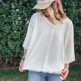 Person wearing a white blouse and beige cap with text, standing outdoors.